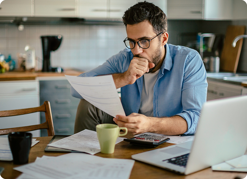 Man sitting at table with papers, a laptop, coffee mug, and a calculator.