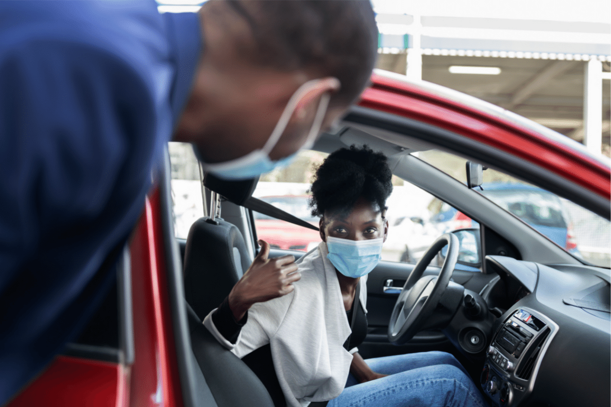 Young man in a face mask getting into a red ride share car.