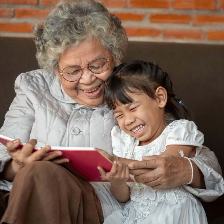 Grandma reading a book and laughing with her granddaughter